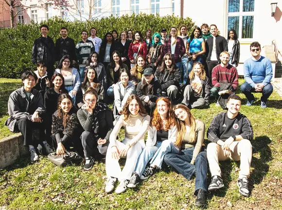 Eine Gruppe von ca. 35 internationalen Studierenden sitzt und steht auf einer Wiese vor dem Verwaltungsgebäude der Universität Erfurt